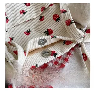 Close-up of strawberry corduroy tote with magnetic silver snap and plush ball detail