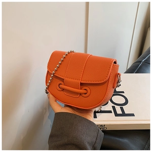 Detail view of orange pebbled leather saddle bag with silver bead chain strap and flap