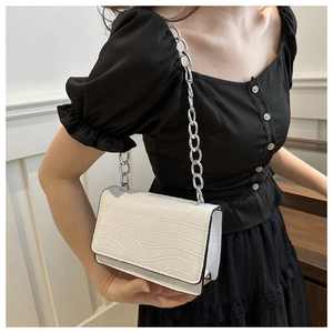Close-up of white crocodile pattern crossbody bag with silver chain on black dress