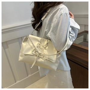 Dettaglio borsa a tracolla beige con fiocco e tracolla a catena in metallo su modella