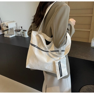 Detail view of large white textured tote bag with black zipper and small matching pouch