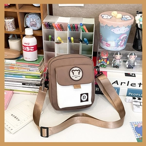 Close-up of canvas messenger bag with brown and white color blocking and cute bear logo