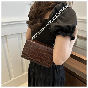Close-up of brown crocodile pattern shoulder bag with shiny finish and silver chain