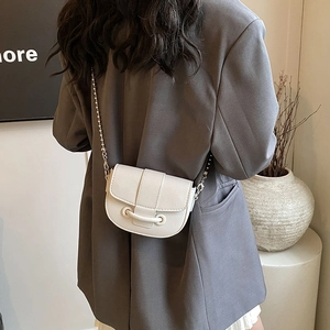 White lychee pattern saddle bag with chain strap worn by a model in a grey suit