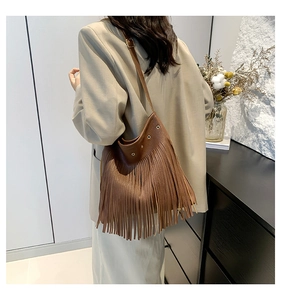 Macro detail of brown leather hobo bag featuring bohemian fringe and metal eyelets