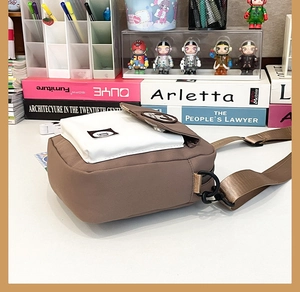 Detail of canvas crossbody bag showing two-tone brown and white design with letter D logo