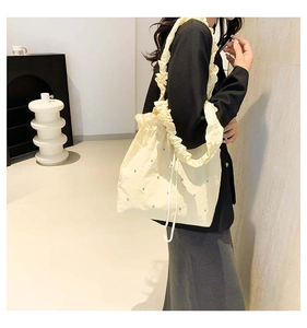 Detail of cream pleated tote bag featuring subtle rhinestone accents and drawstring closure