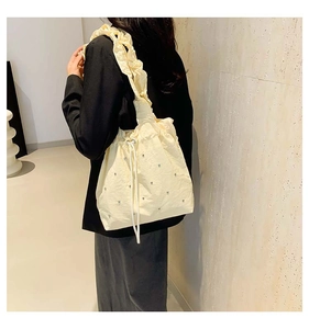 Detail of light yellow pleated tote bag with drawstring closure and metal heart accents