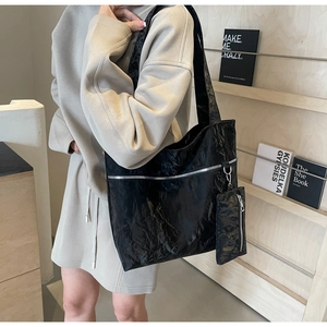 Detail of black glossy tote bag with silver zipper and small pouch on a model