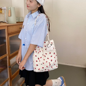 Corduroy tote bag with strawberry prints and plush charm worn by a stylish woman