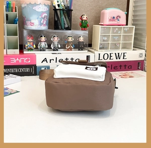 Close-up of brown canvas crossbody bag with white pocket flap and black round logo detail