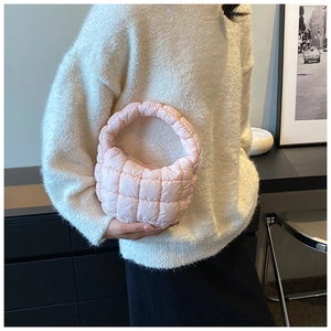 Detailed view of pink quilted cloud bag carried by a model in a cozy knit sweater