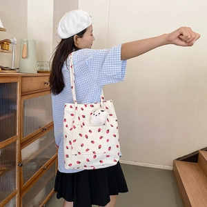 Detail of white corduroy strawberry tote bag with front pocket and plush bear pendant