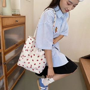 Detail of corduroy tote bag with strawberry prints and a plush bear keychain accessory
