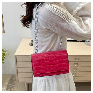 Detail of fuchsia crocodile pattern crossbody bag with a silver chain strap for women