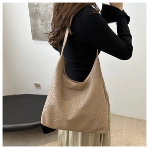 Detailed view of brown woven tote bag on shoulder showing large capacity and stylish texture