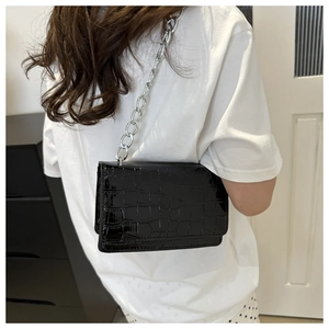 Detail showing the black crocodile pattern texture and silver chain strap of the bag