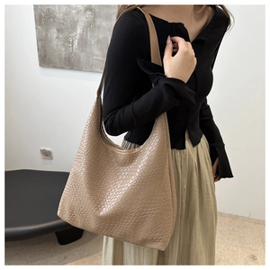 Detailed texture view of beige embossed leather tote bag worn on a model's shoulder