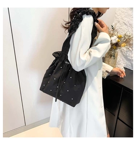 Detail of black drawstring tote bag with silver studs and ruffled shoulder strap