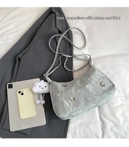 Borsa tote grigio argento a pieghe con farfalla in metallo e charm accanto a un iPad