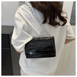 Detail of black croc-embossed patent leather bag with thick silver metal chain strap