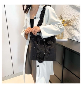 Detail of black pleated tote bag with white pearl accents and ruffled shoulder strap