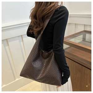 Detail of a large woven tote bag in dark coffee brown with an intricate Intrecciato pattern