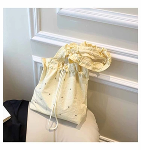 Close-up of pale yellow pleated tote bag with silver studs and ruffled shoulder strap detail