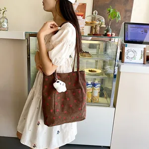 Detail view of a corduroy strawberry tote bag with a plush cloud charm in a cafe setting