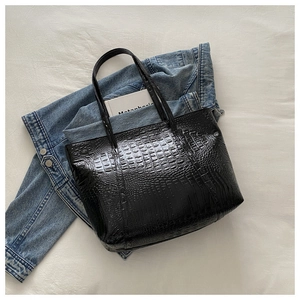 Macro shot of black crocodile embossed tote bag with glossy finish on soft fabric background
