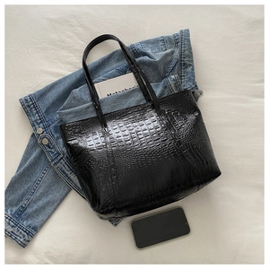 Detail of black faux crocodile leather tote bag with glossy texture on white background