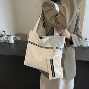 Large white minimalist tote bag with small zipper pouch shown on shoulder by model