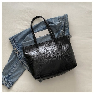 Close-up of black crocodile pattern leather tote bag placed on a blue denim jacket