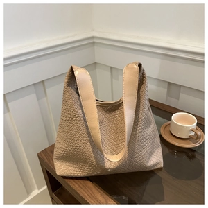 Detail of light khaki woven texture tote bag with flat leather shoulder strap on a wooden table