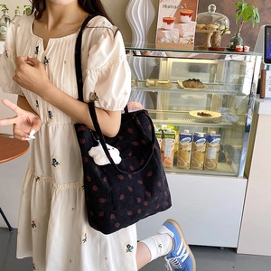 Detail of black corduroy tote bag with strawberry print and plush cloud charm accessory