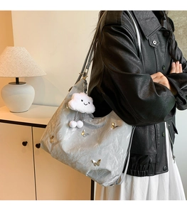 Détail d'un sac cabas argenté avec charmes papillon et porte-clés en peluche nuage