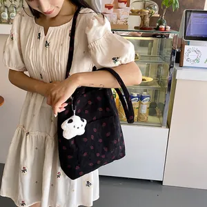 Detail of black corduroy strawberry tote bag with white plush charm and embroidery