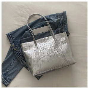 Detail of silver crocodile pattern tote bag shown on denim jacket for casual style