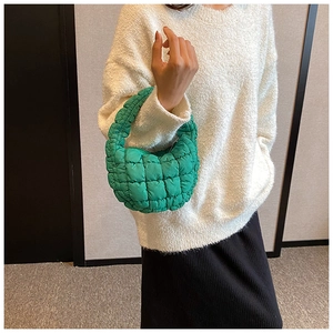 Detail of green puffy quilted handbag with knotted handle on a white sweater background