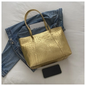 Macro view of gold metallic tote bag featuring crocodile embossed texture and dual handles