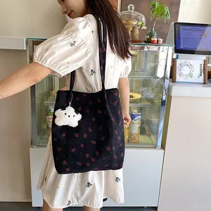Detail of black corduroy strawberry tote bag with plush star pendant worn on shoulder