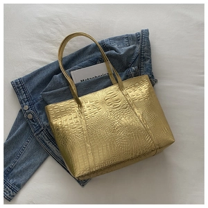 Flat lay of gold tote bag with crocodile pattern over denim jacket on white fabric