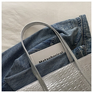 Detail of silver crocodile pattern tote bag shown with casual denim and a book