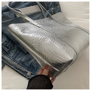 Detailed side view of large silver tote bag with textured crocodile pattern on denim