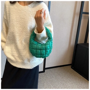 Close-up of vibrant green quilted puffy cloud handbag held against a minimal outfit