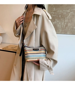 Close-up of rainbow striped woven shoulder bag with black leather logo patch and strap