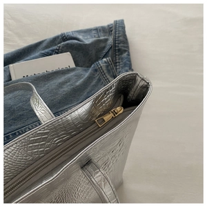 Macro shot of silver crocodile embossed tote bag with gold zipper and gray lining detail