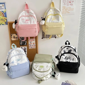 Detail view of five nylon backpacks in pink, yellow, blue, green, and black with cute pendants