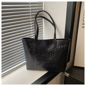 Close-up of black glossy crocodile embossed tote bag with slim dual top handles