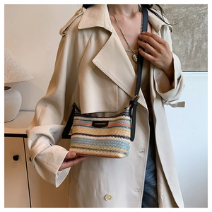 Detail of colorful woven rainbow straw crossbody bag worn with a beige trench coat